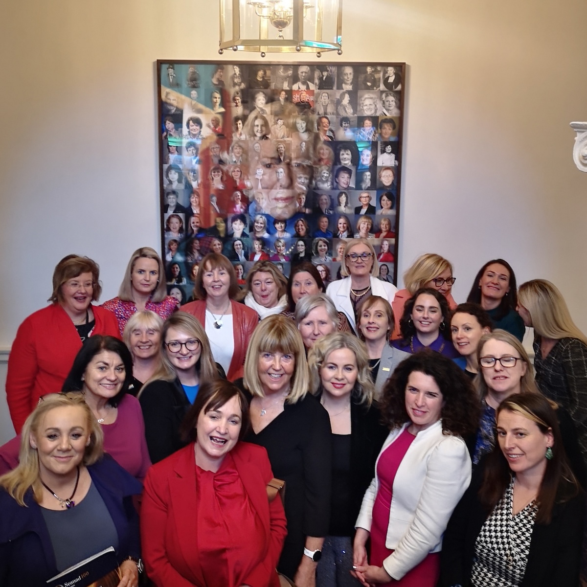 Mary Kelly: Women in Seanad Éireann 1922 to 2022, 175 x 150cm, 2022; installation view with current women senators in the Seanad, plus the artist, third from the left, in black, standing in front of the artwork, looking towards the camera